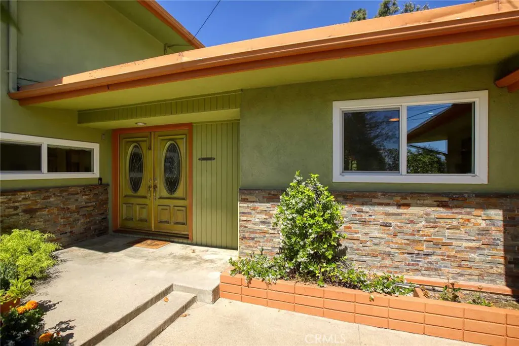 Exterior of a green house with a double front door, stone accents, and a concrete walkway.