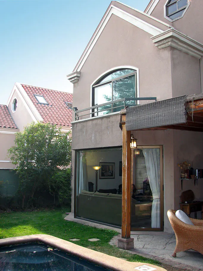 Backyard view of a two-story beige house with a pool, green lawn, patio, and large windows.