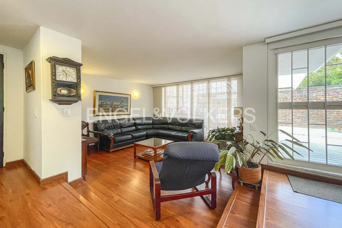 Living room with hardwood floors, black leather sectional, blue armchair, wooden coffee table, and a wall-mounted clock.