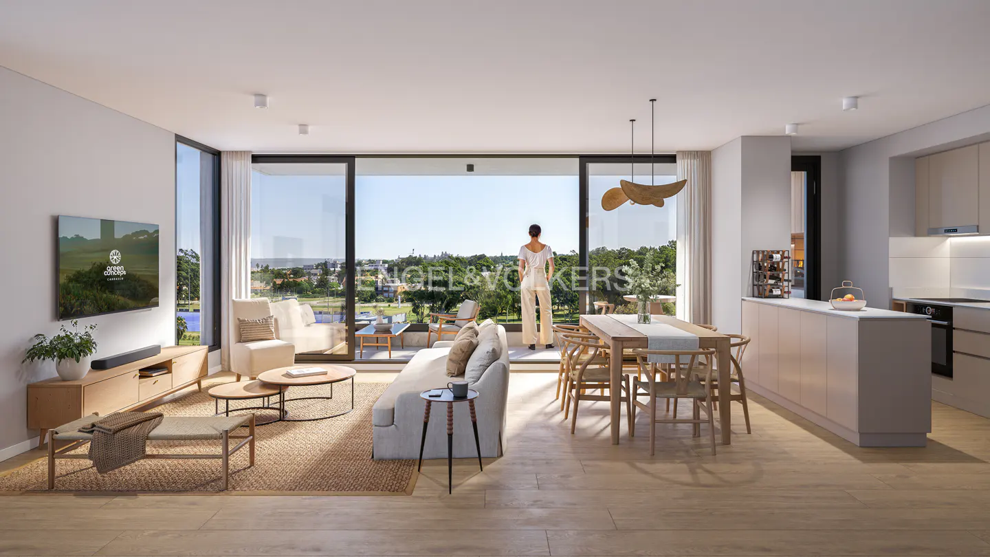 Bright, modern apartment interior with a woman looking out a large window at a green landscape. Neutral tones, wood floors, and sleek furniture.