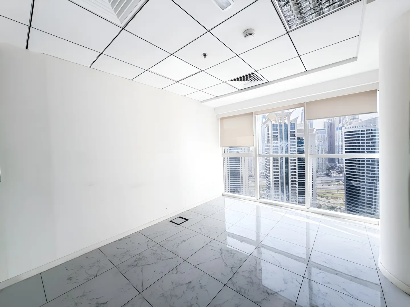 Empty office space with white walls, marble tile floor, and large windows overlooking a city skyline.