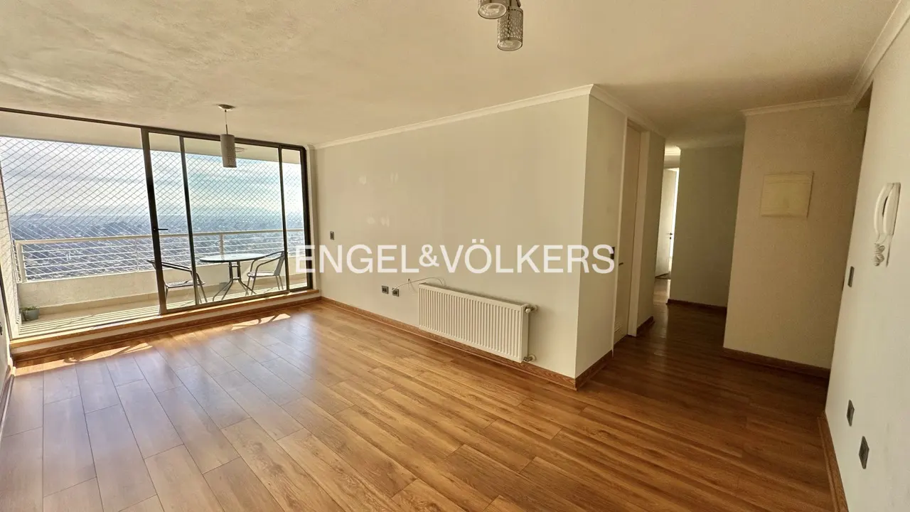 Bright, empty apartment with wood floors, white walls, and a balcony with city views. Engel & Völkers logo on the wall.