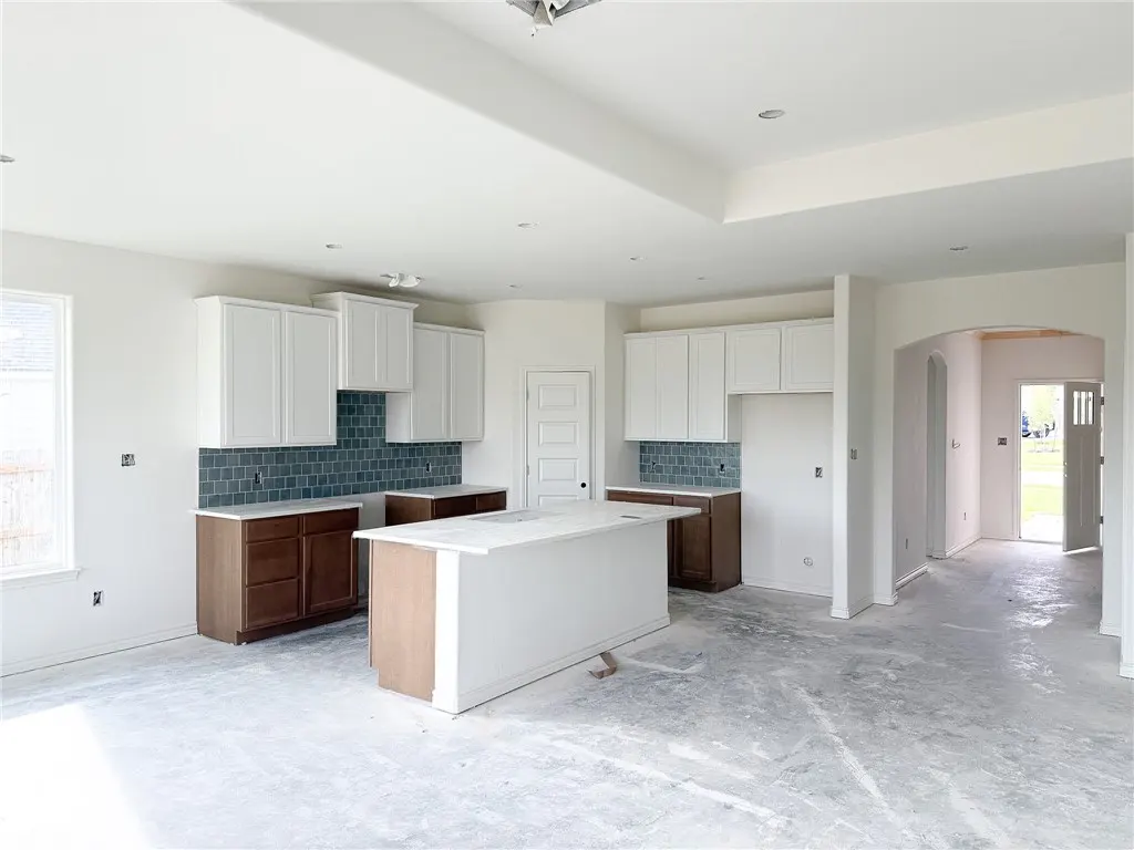 Modern kitchen under construction with white upper cabinets, brown lower cabinets, a central island, and blue tile backsplash.