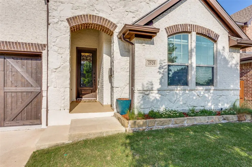 Exterior view of a white stone house with a brown door, brick archway, and green lawn. The house number "2520" is visible above a window.