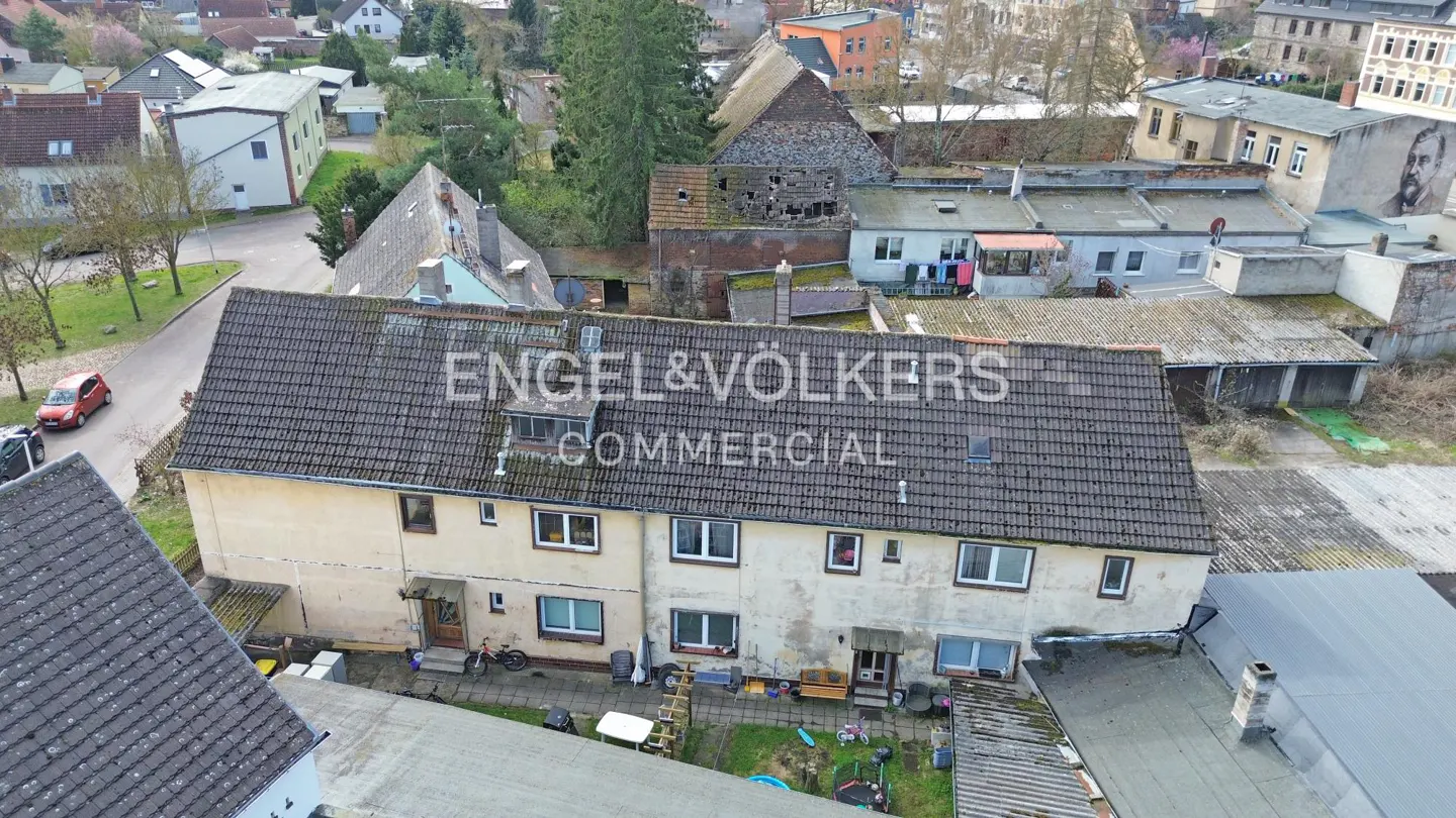 Aerial view of a row of attached, two-story, beige buildings with a dark gray tiled roof and the Engel & Völkers logo.