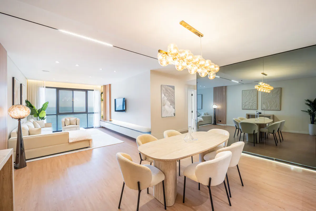 Modern open-plan living and dining area with light wood floors, cream furniture, and a large mirror wall reflecting the room.