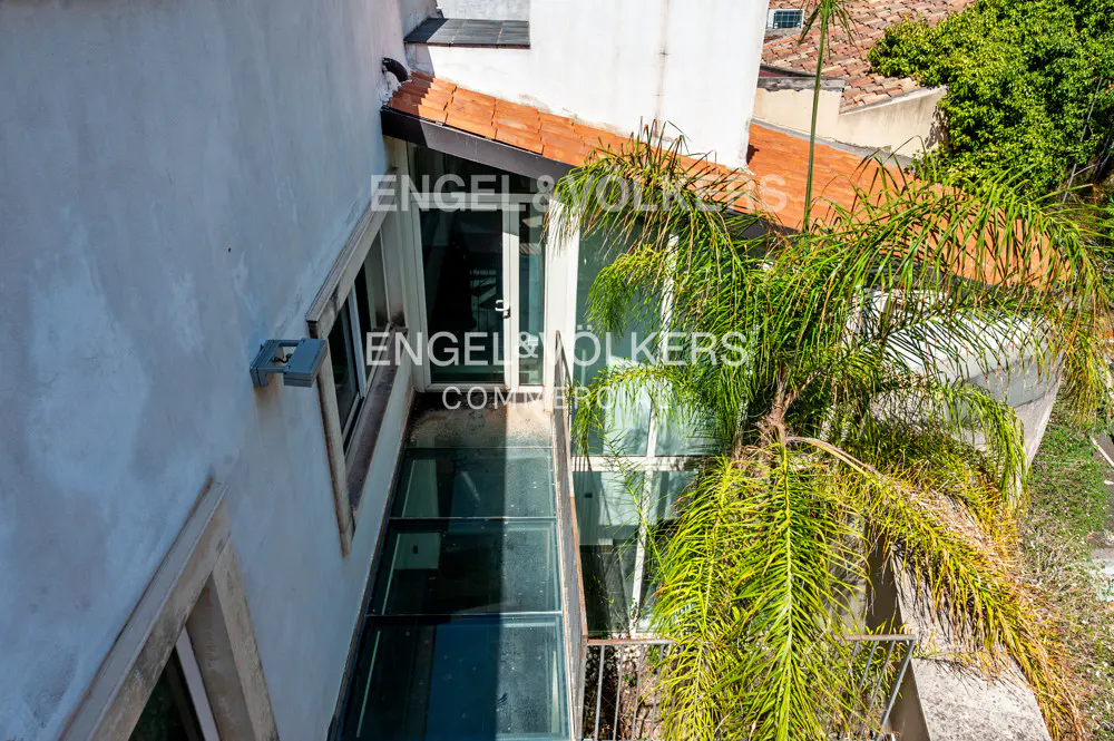 Exterior view of a building with a glass-floored balcony and a palm tree, showcasing Engel & Völkers branding.