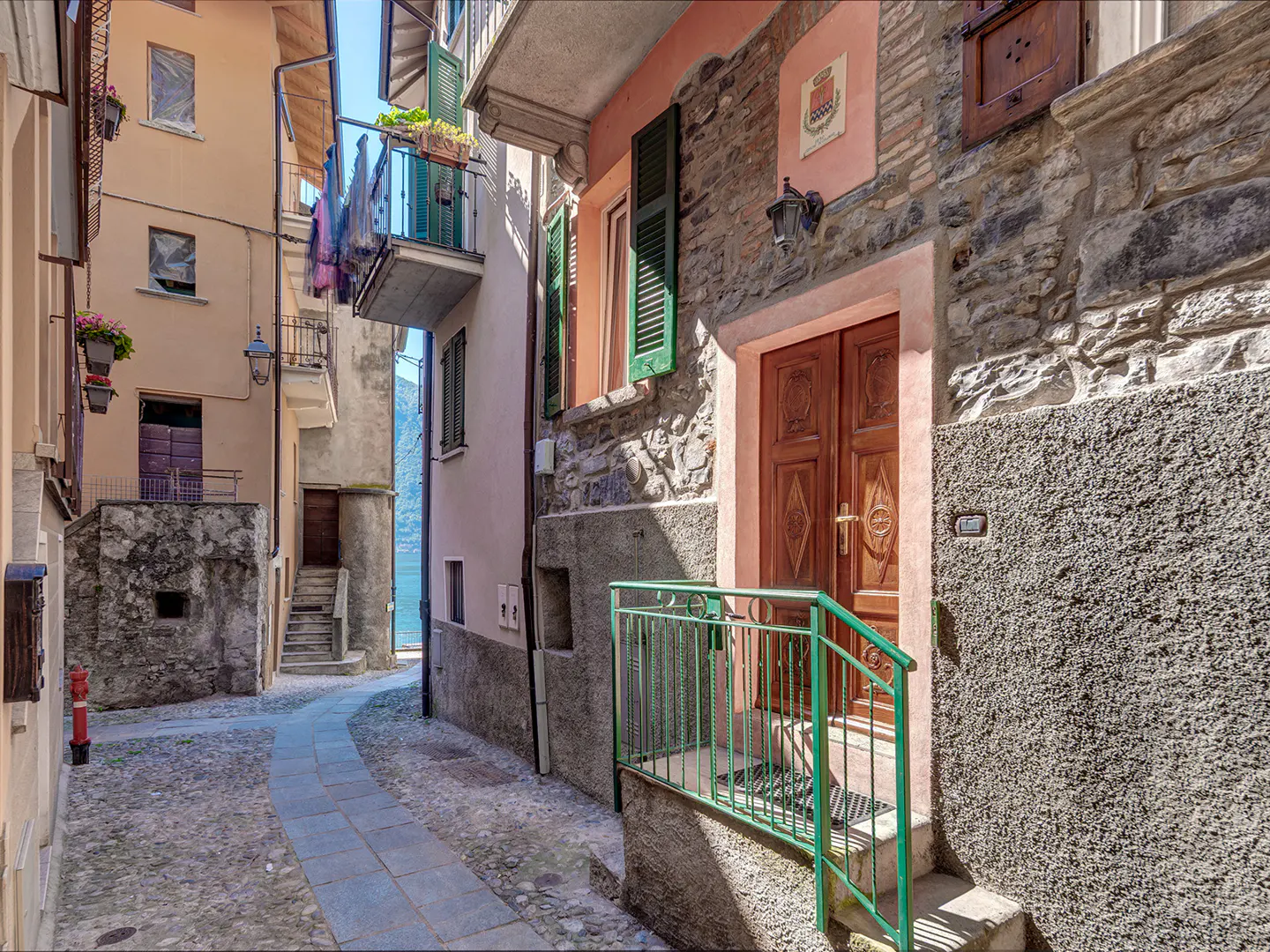 Cobblestone street view in Italy with stone buildings, green shutters, and a wooden door with a green railing.