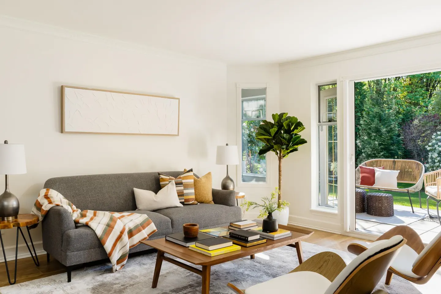 Bright living room with gray sofa, wood coffee table with books, and open patio doors to a green garden.