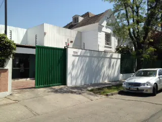 Exterior view of a white house with a green gate and a silver car parked on the street.