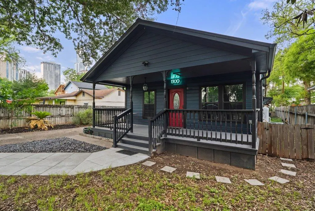 A dark blue house with a red door and a porch with black railings. A green neon sign reads "1300" above the door.