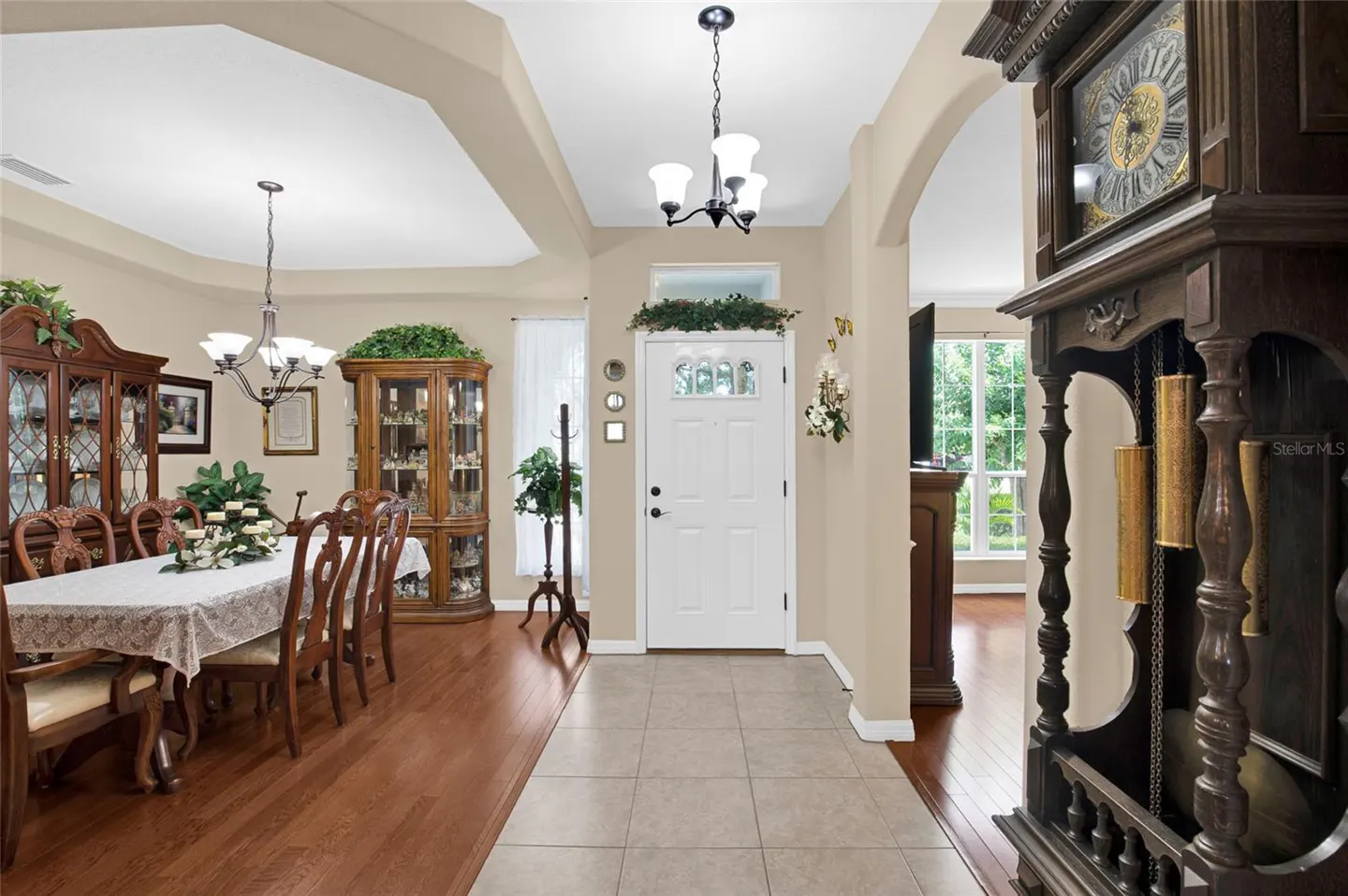 Dining room with wood floors, a table set for six, and a white front door in the background with a tall grandfather clock.