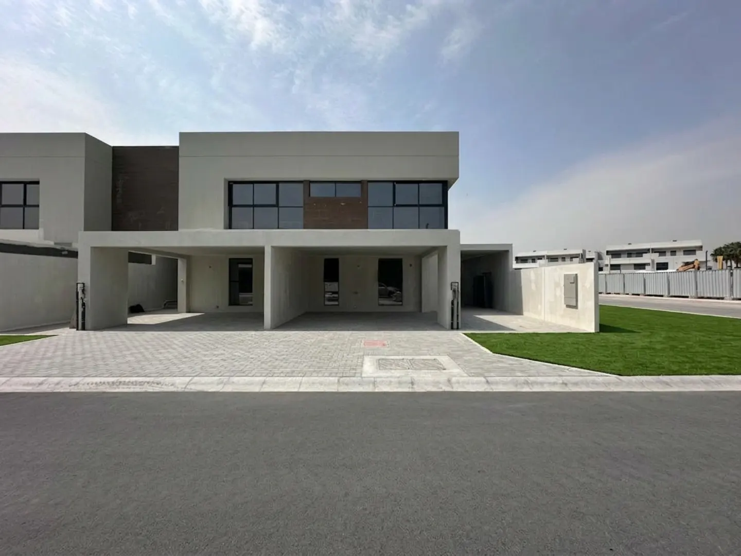 Modern two-story house with a gray facade, black windows, and a covered parking area. Paved driveway and green lawn in front.