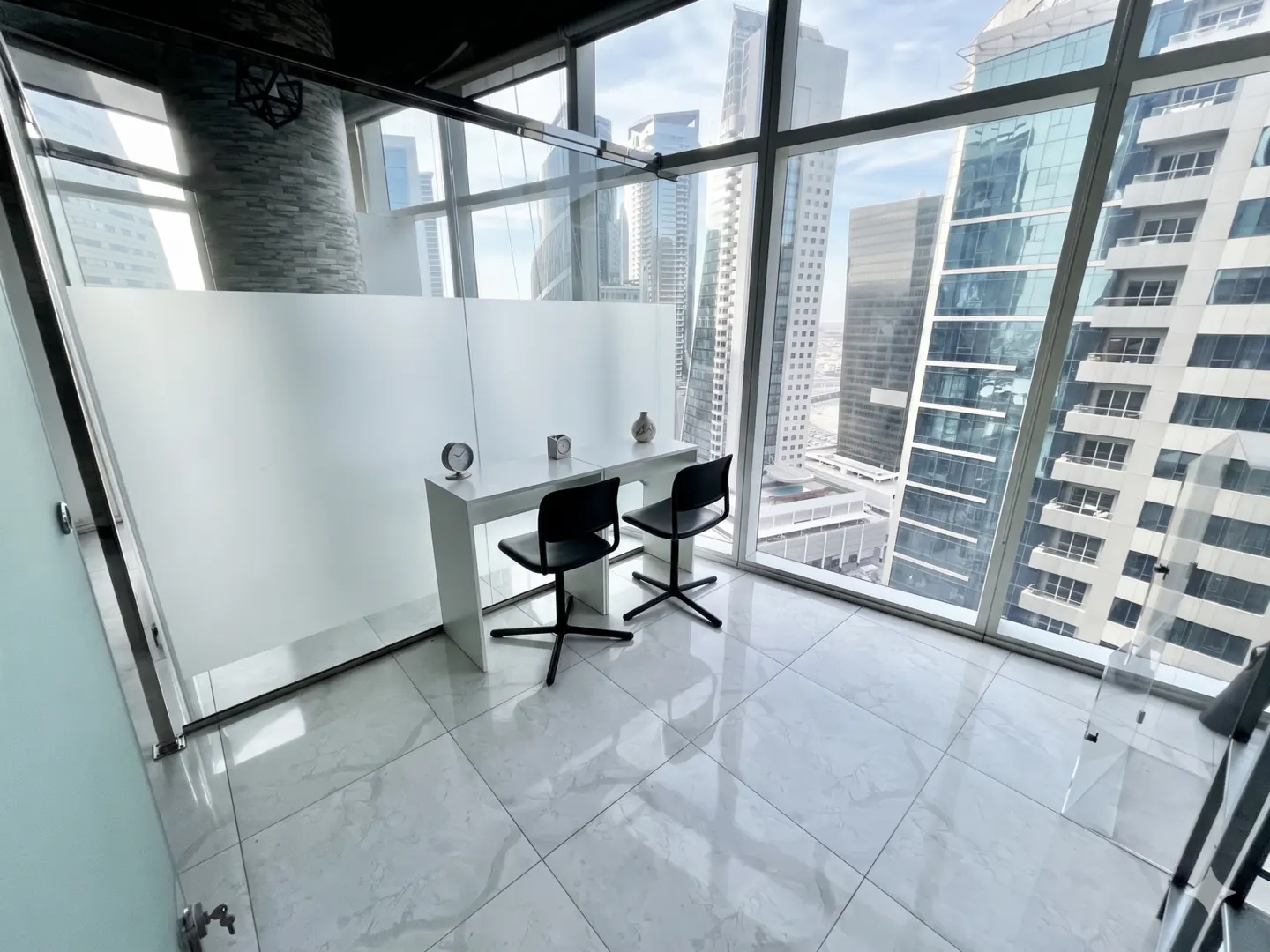 A modern office space with a white desk, two black chairs, and a large window overlooking a city skyline. The floor is white marble.