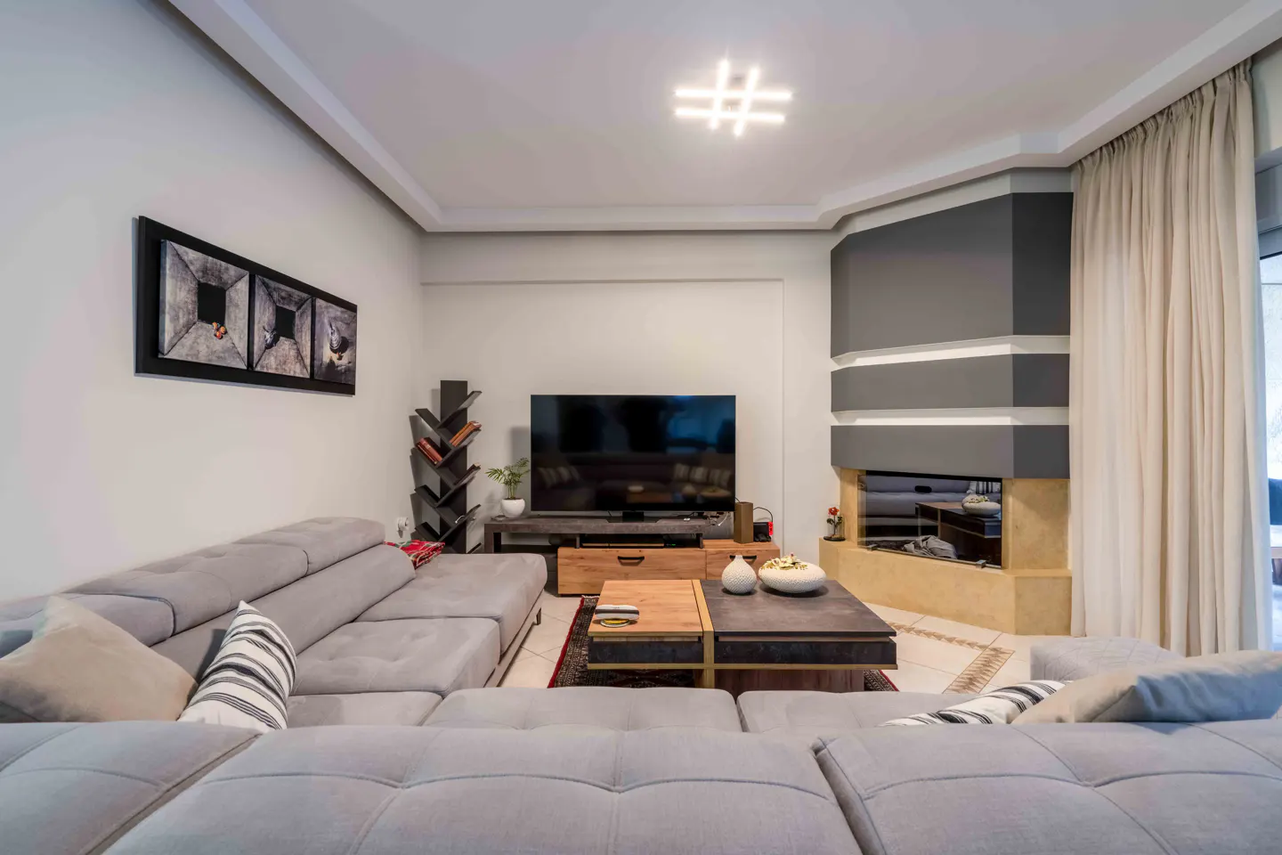 Living room with a gray sectional sofa, a TV, a gray fireplace, and a modern light fixture.