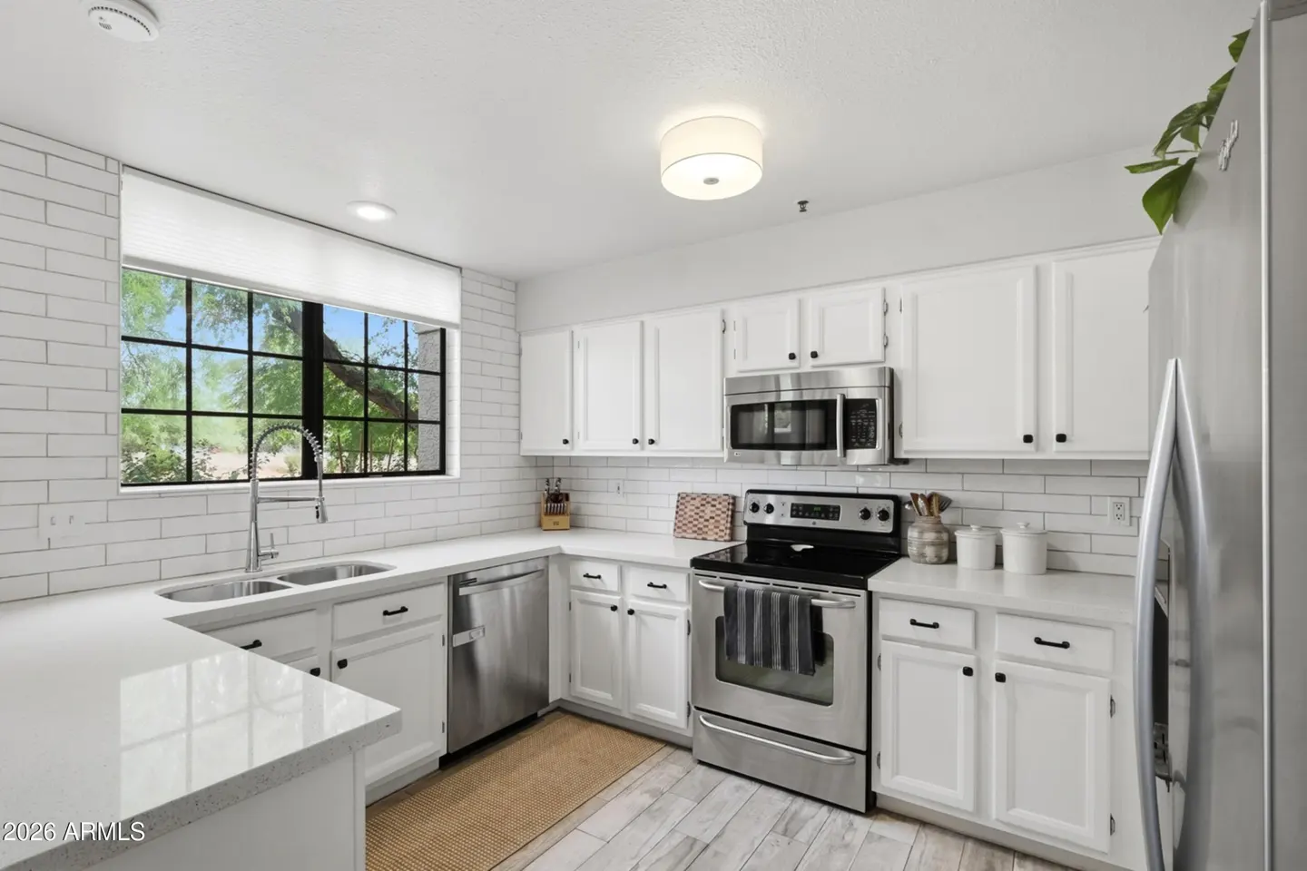 Bright, white kitchen with stainless steel appliances, white cabinets, and a large window overlooking greenery.