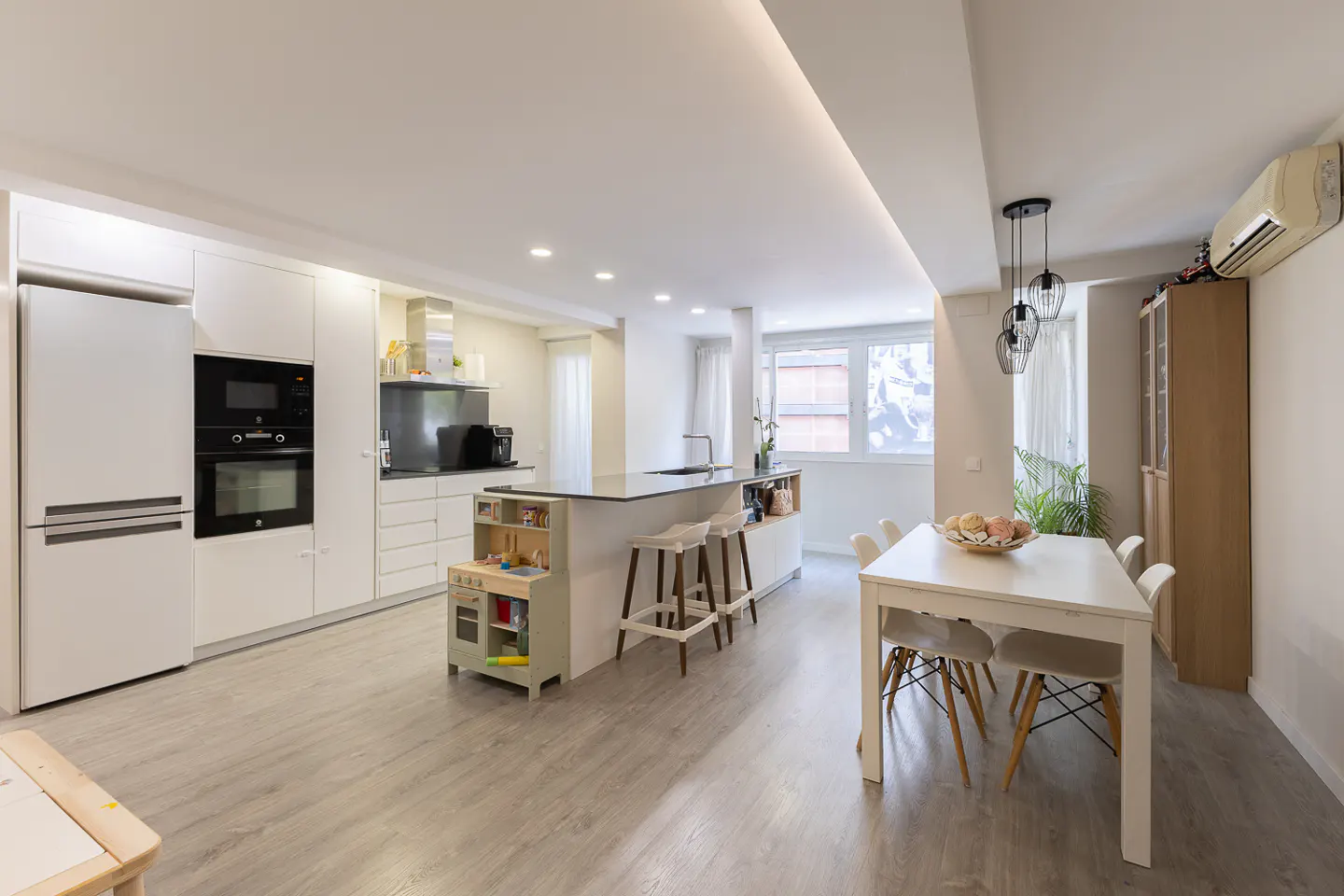 Bright, open-concept kitchen and dining area with white cabinets, island with stools, and a white dining table with chairs.