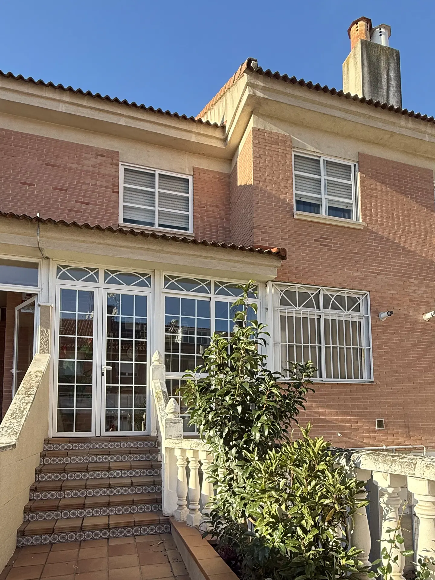 Exterior view of a two-story brick house with white-framed windows, a tiled roof, and a chimney against a blue sky.