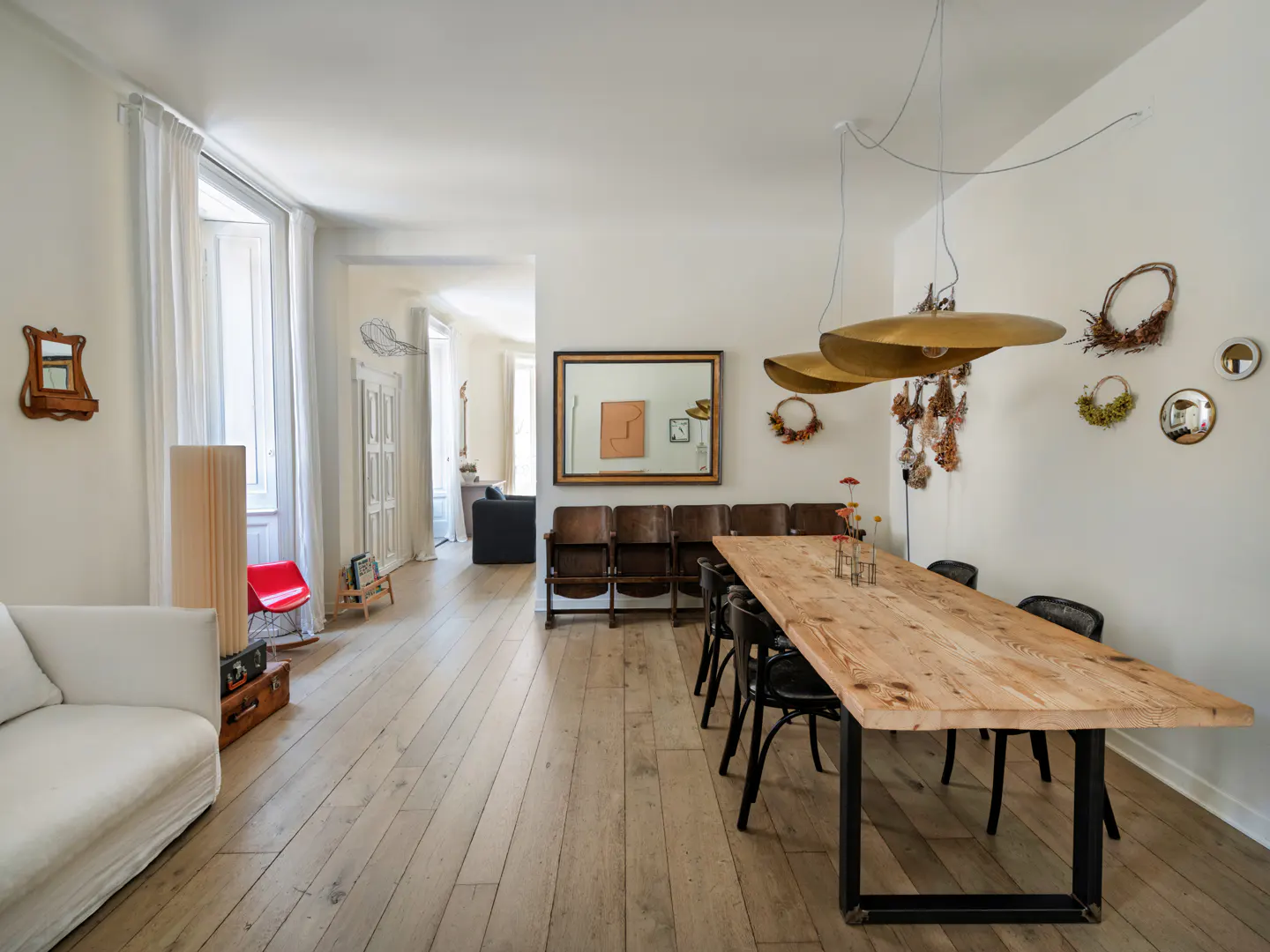 Bright dining room with a long wooden table, black chairs, gold pendant lights, and white walls with decorative mirrors.