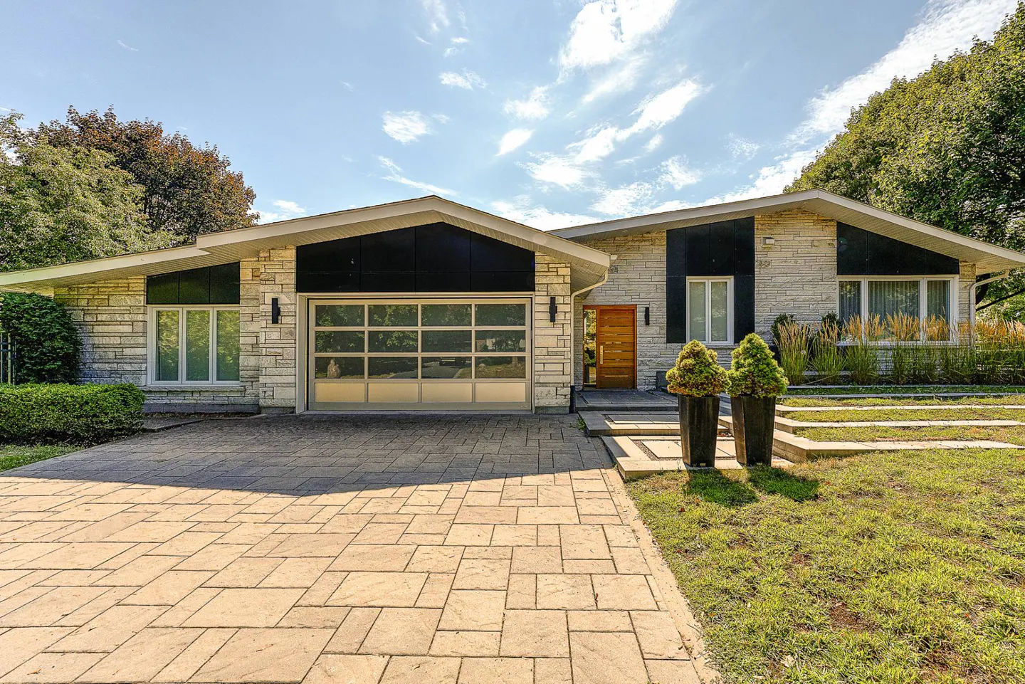 Exterior of a stone house with a glass garage door and a brick driveway.