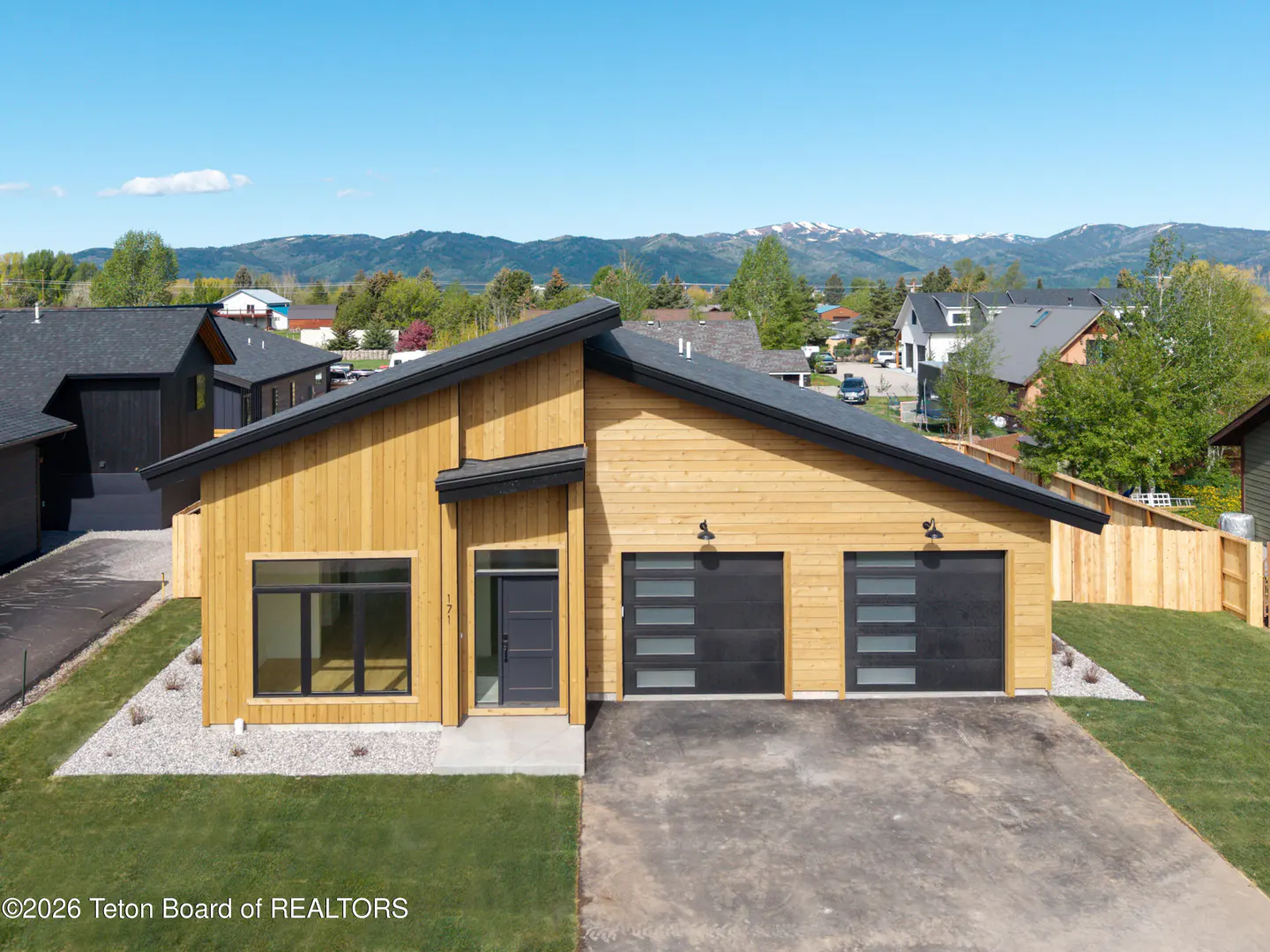Modern, light-wood home with a black roof and two-car garage. Mountains are visible in the background.