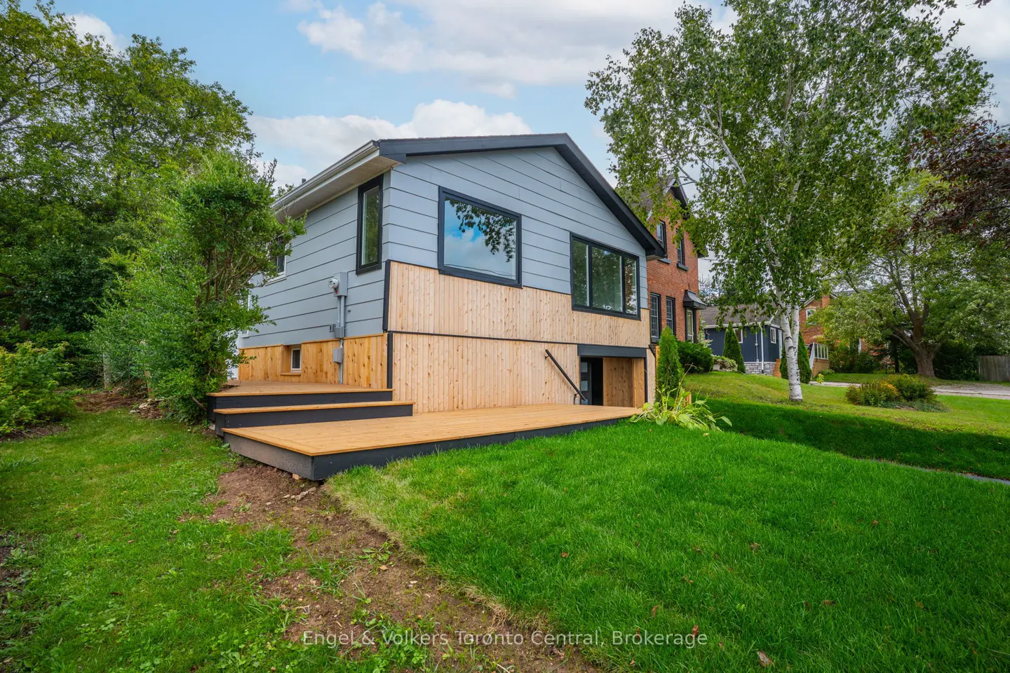 Exterior view of a two-story house with light blue siding, a wooden deck, and a green lawn.