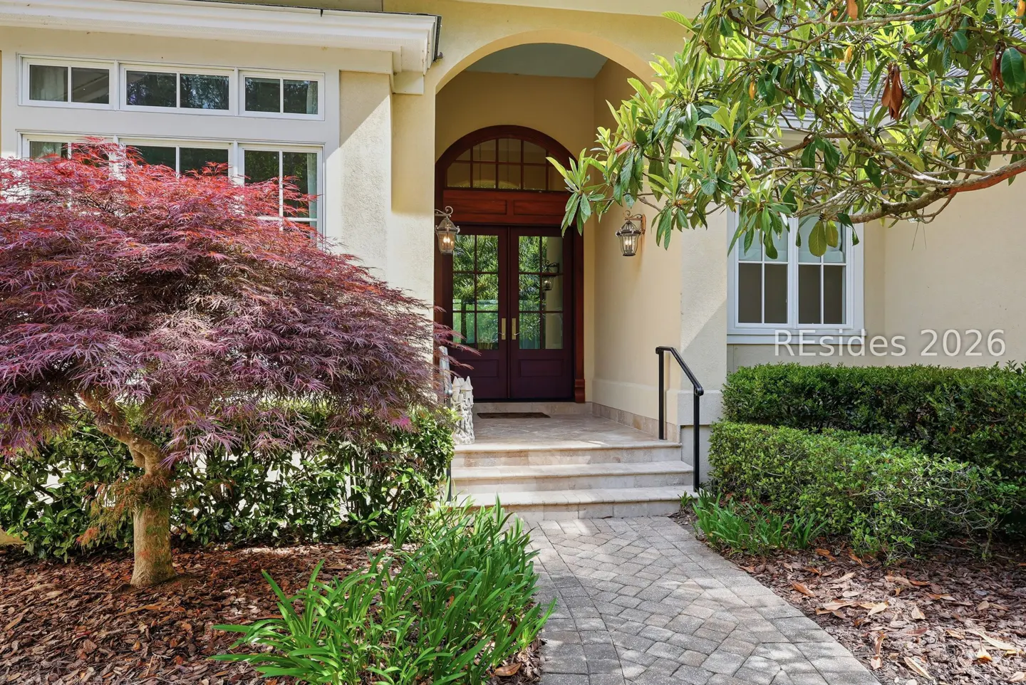 Front entrance of a beige house with a red Japanese maple tree and a stone walkway.