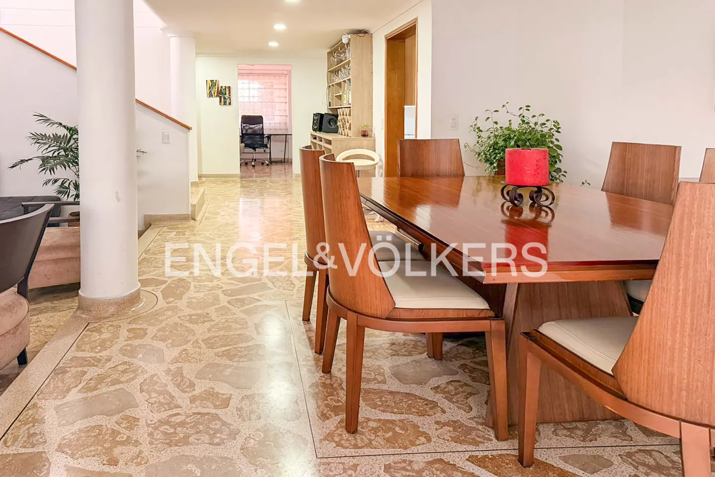 A dining room with a long wooden table and chairs, a red candle, and a stone floor.