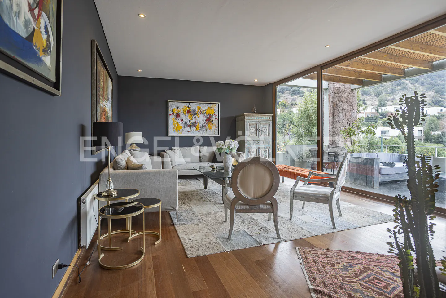 Modern living room with dark gray walls, light sofas, a glass coffee table, and floor-to-ceiling windows overlooking a patio.