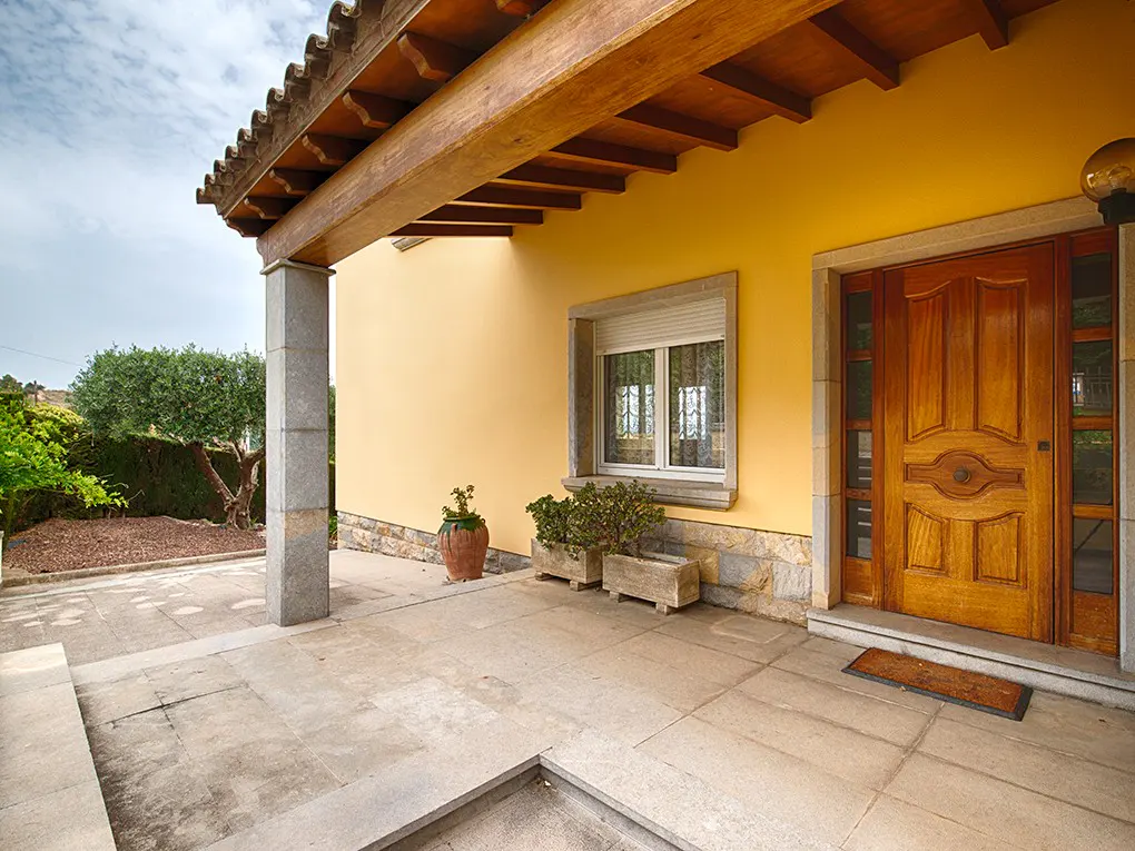 Exterior view of a yellow house with a wooden door, stone accents, and a tiled porch.