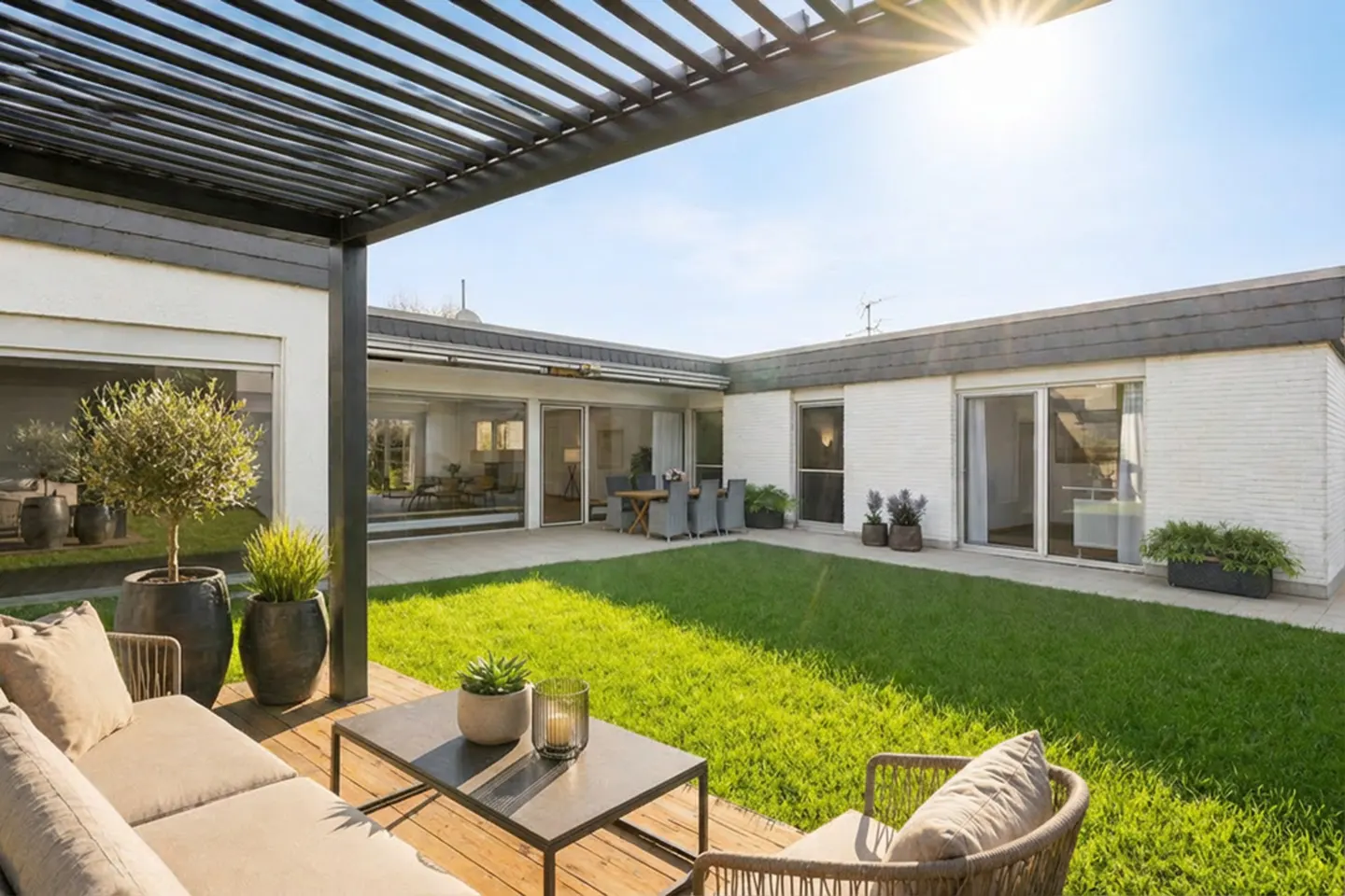 Outdoor patio with a pergola, a beige couch, a black table, and a green lawn surrounded by a white brick house.