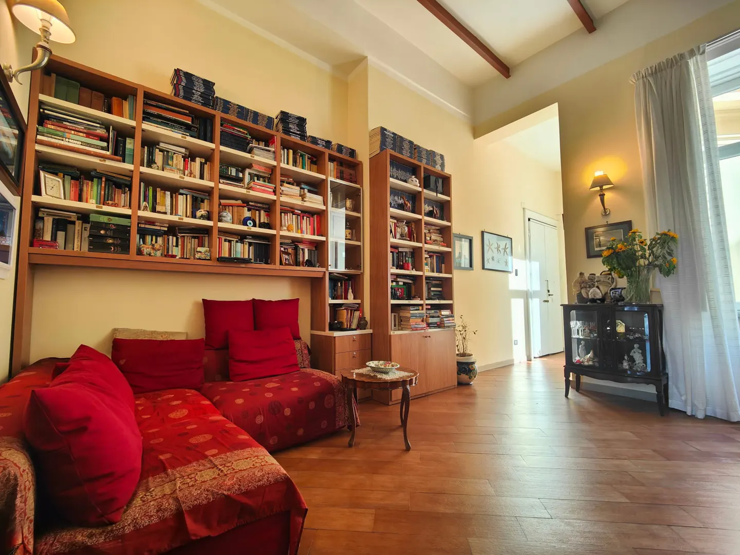 A living room with hardwood floors, a red couch, and floor-to-ceiling bookshelves filled with books.