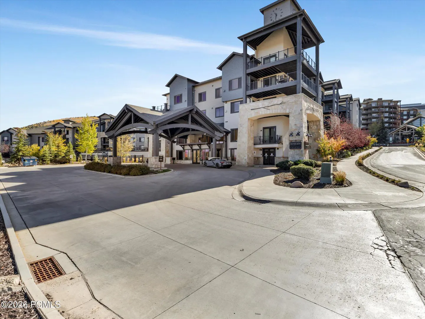 Exterior view of a gray condo building with a clock tower and a covered entrance. A car is parked at the entrance.