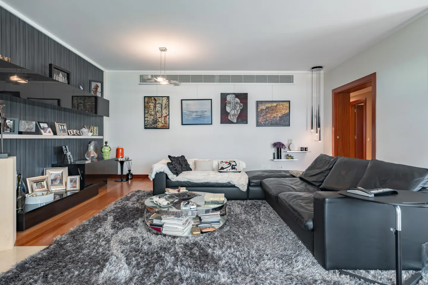 A modern living room with a black leather sectional sofa, gray rug, and artwork on the wall.