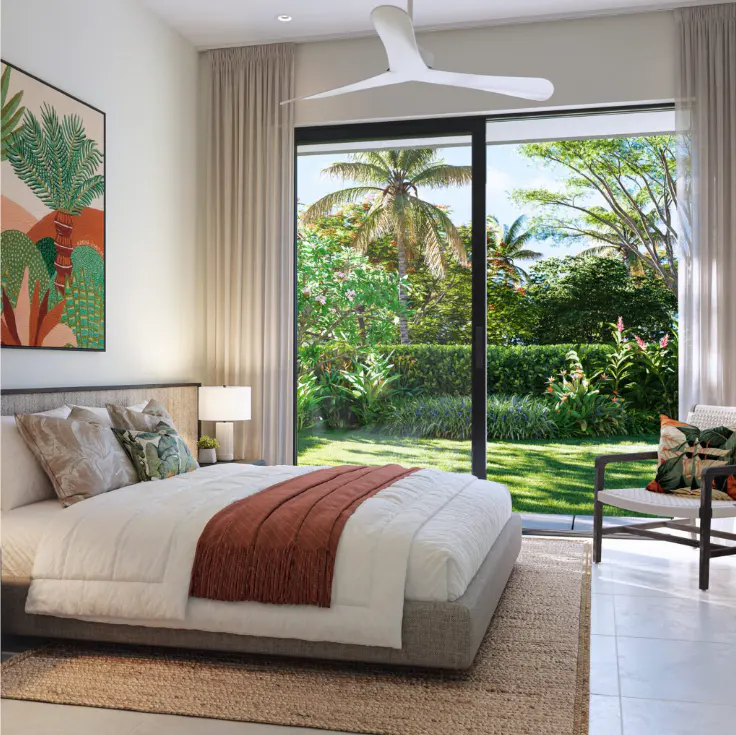 Bedroom with a large bed, white linens, and a rust-colored throw. A large window overlooks a lush green garden. A white ceiling fan is visible.