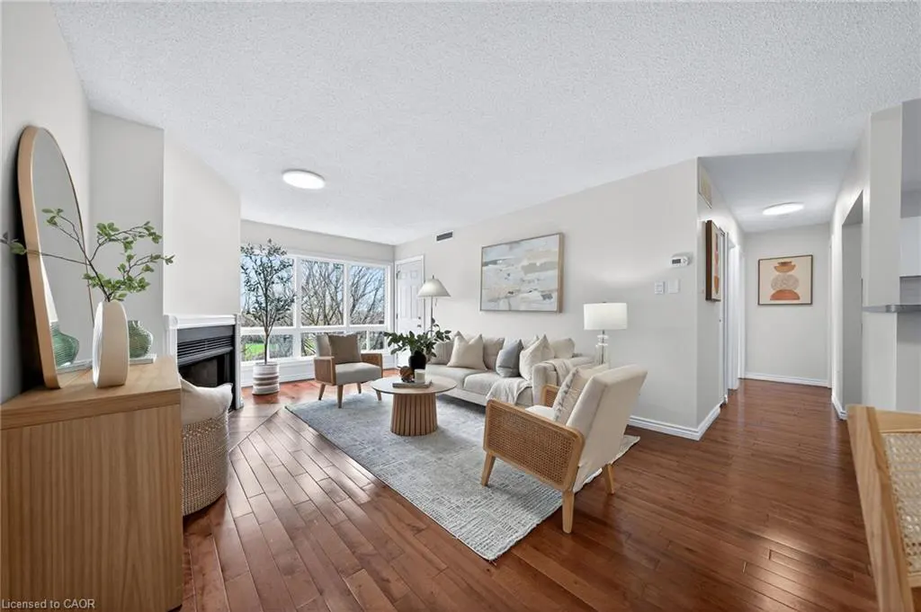 Bright living room with hardwood floors, a fireplace, and large windows. A sofa, chairs, and a round coffee table furnish the space.