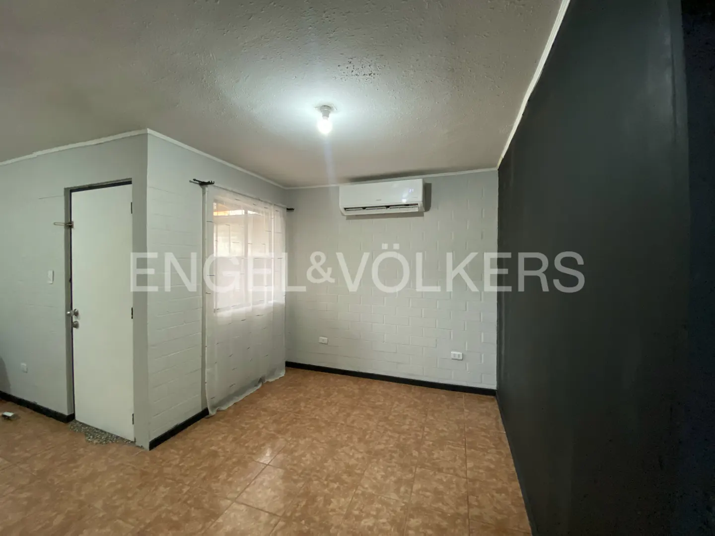 A room with tile floors, a door, a window with sheer curtains, and an air conditioner. The Engel & Völkers logo is visible.