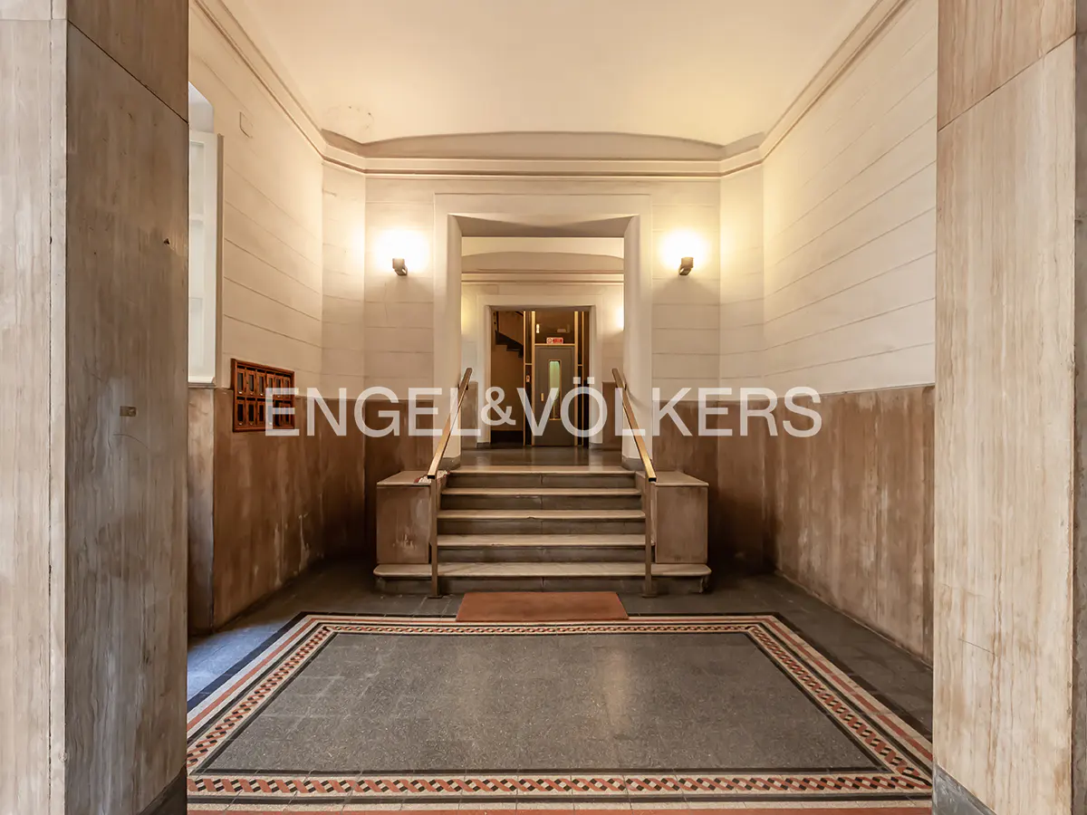 A building's entrance hall with marble walls, a tiled floor, and stairs leading to a doorway.