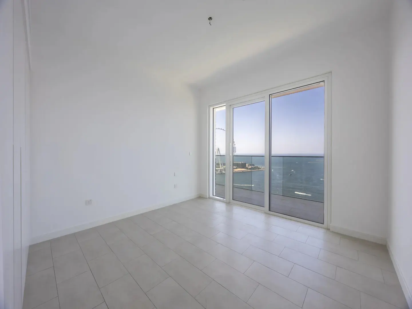 Empty white room with light tile floors and large sliding glass doors opening to a balcony with a scenic ocean view.