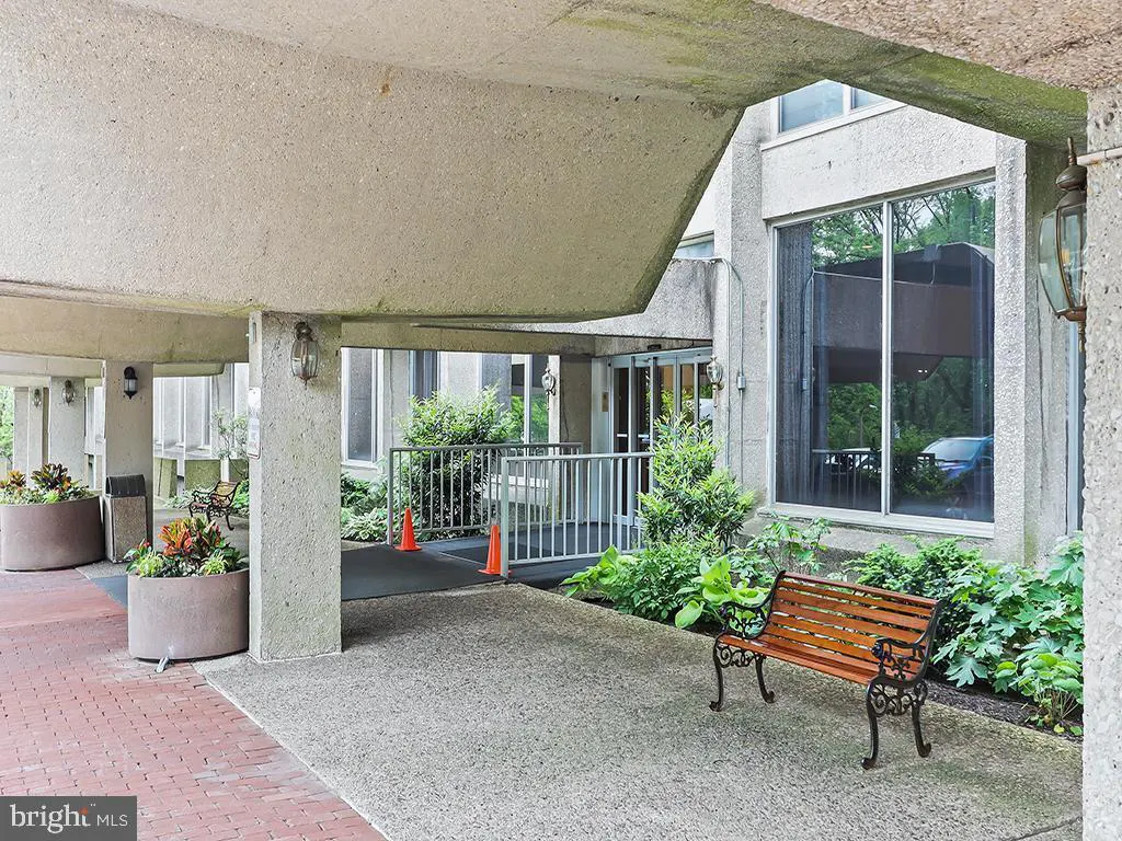 Exterior view of a building entrance with a concrete overhang, planters, and a wooden bench.