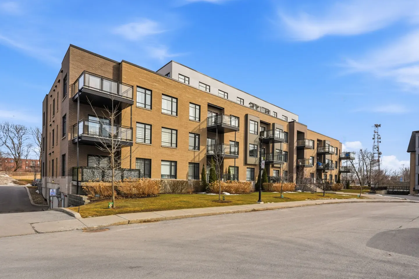 Exterior view of a modern, multi-story brick apartment building with black framed windows and balconies under a blue sky.