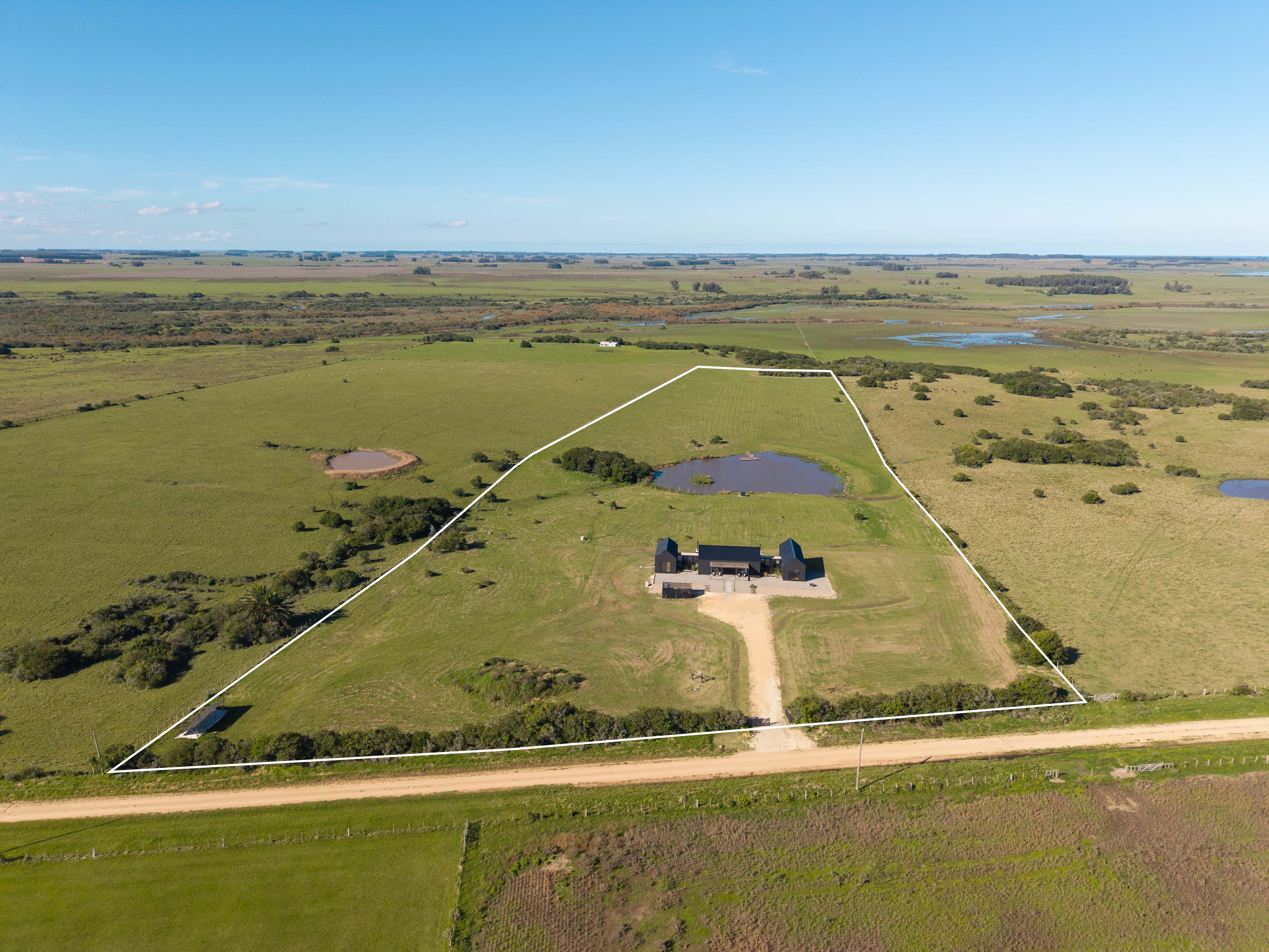 Aerial view of a modern black house with a pond, surrounded by a green field and a white boundary line.