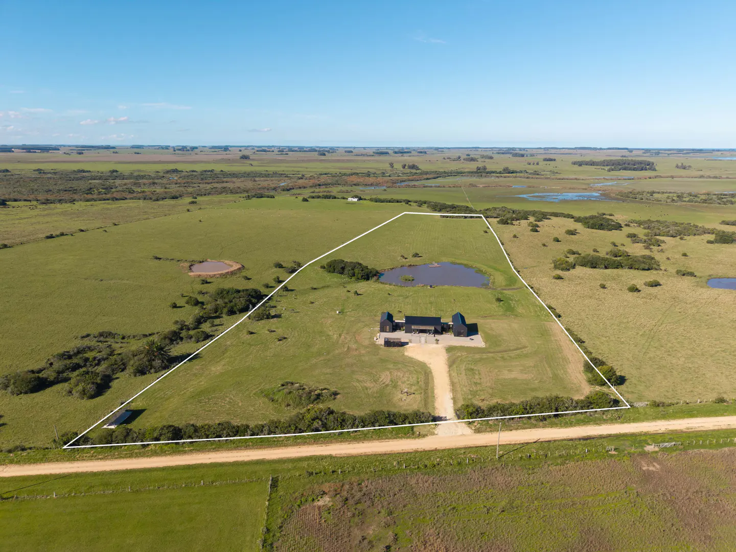 Aerial view of a modern black house with a pond, surrounded by a green field and a white boundary line.
