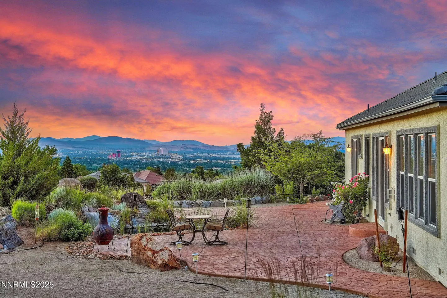 Backyard patio with table and chairs overlooking a city skyline at sunset with pink and orange clouds.