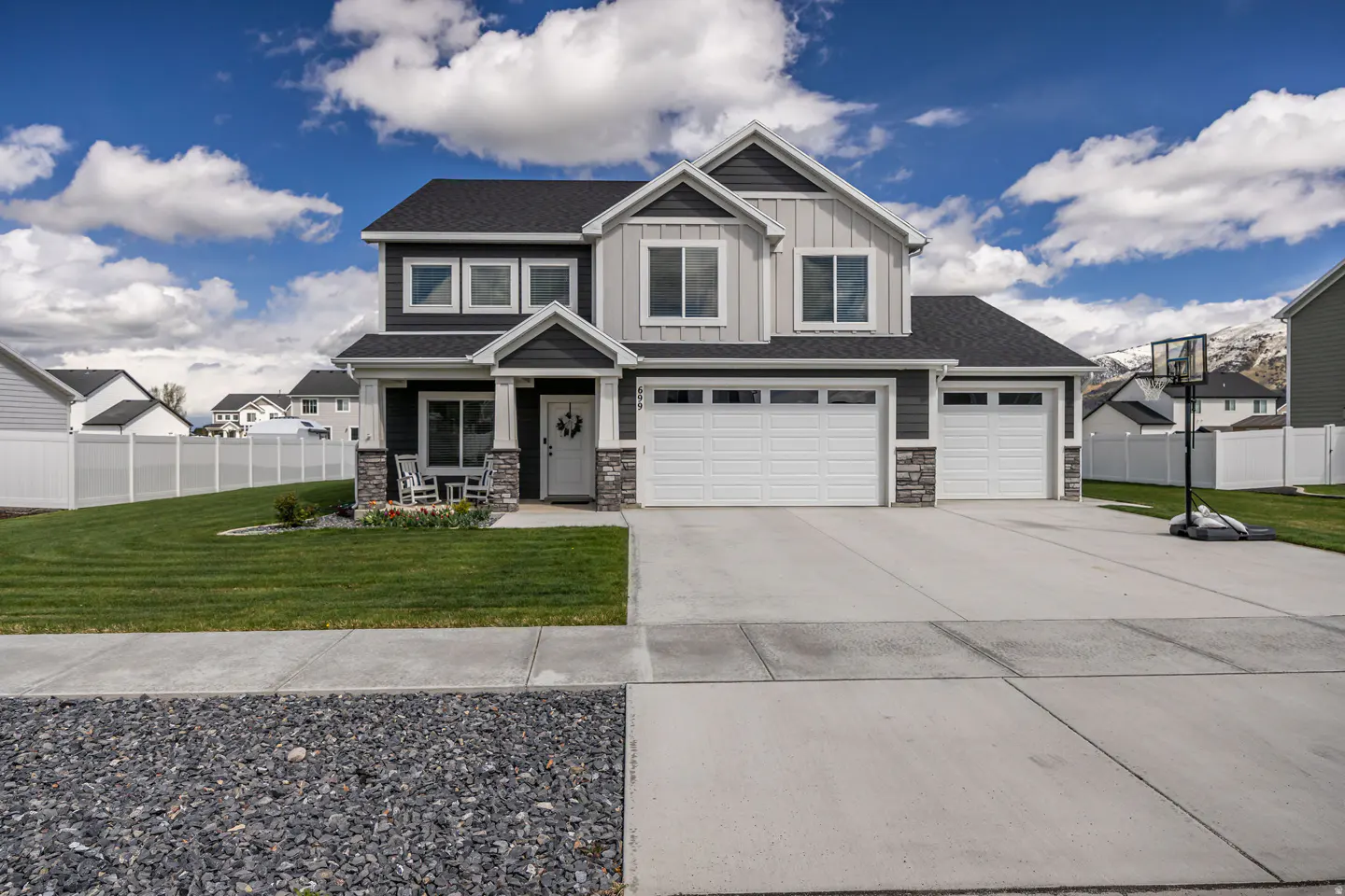 Two-story house with gray and dark gray siding, white trim, and a two-car garage. Green lawn, blue sky with clouds.