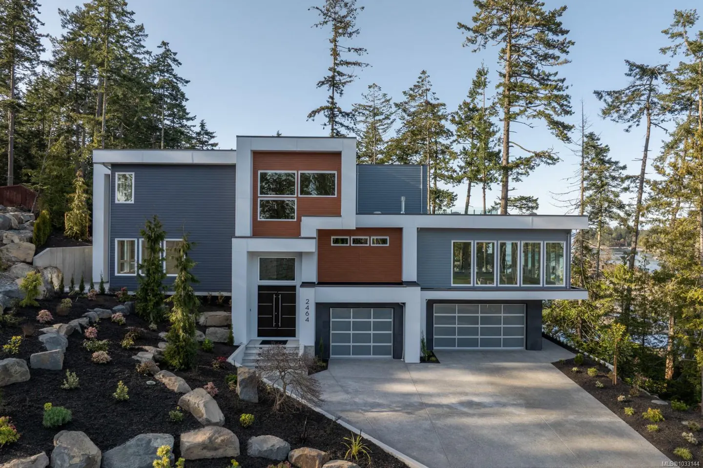 Modern two-story home with gray siding, wood accents, white trim, and two-car garage. Landscaped yard with trees.