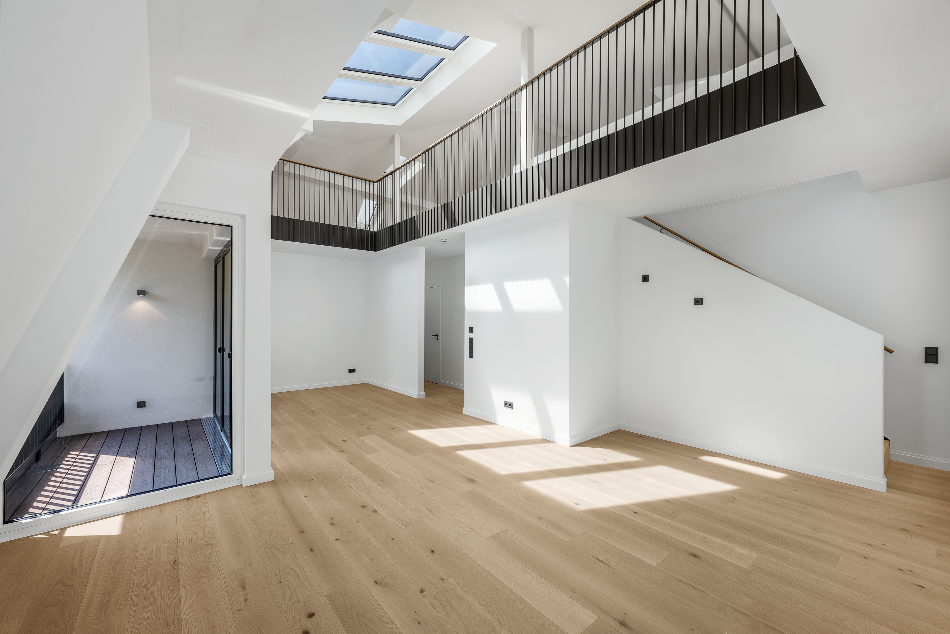 Bright, modern living space with light wood floors, a mezzanine level with black railings, and a skylight above. [AI-generated text]