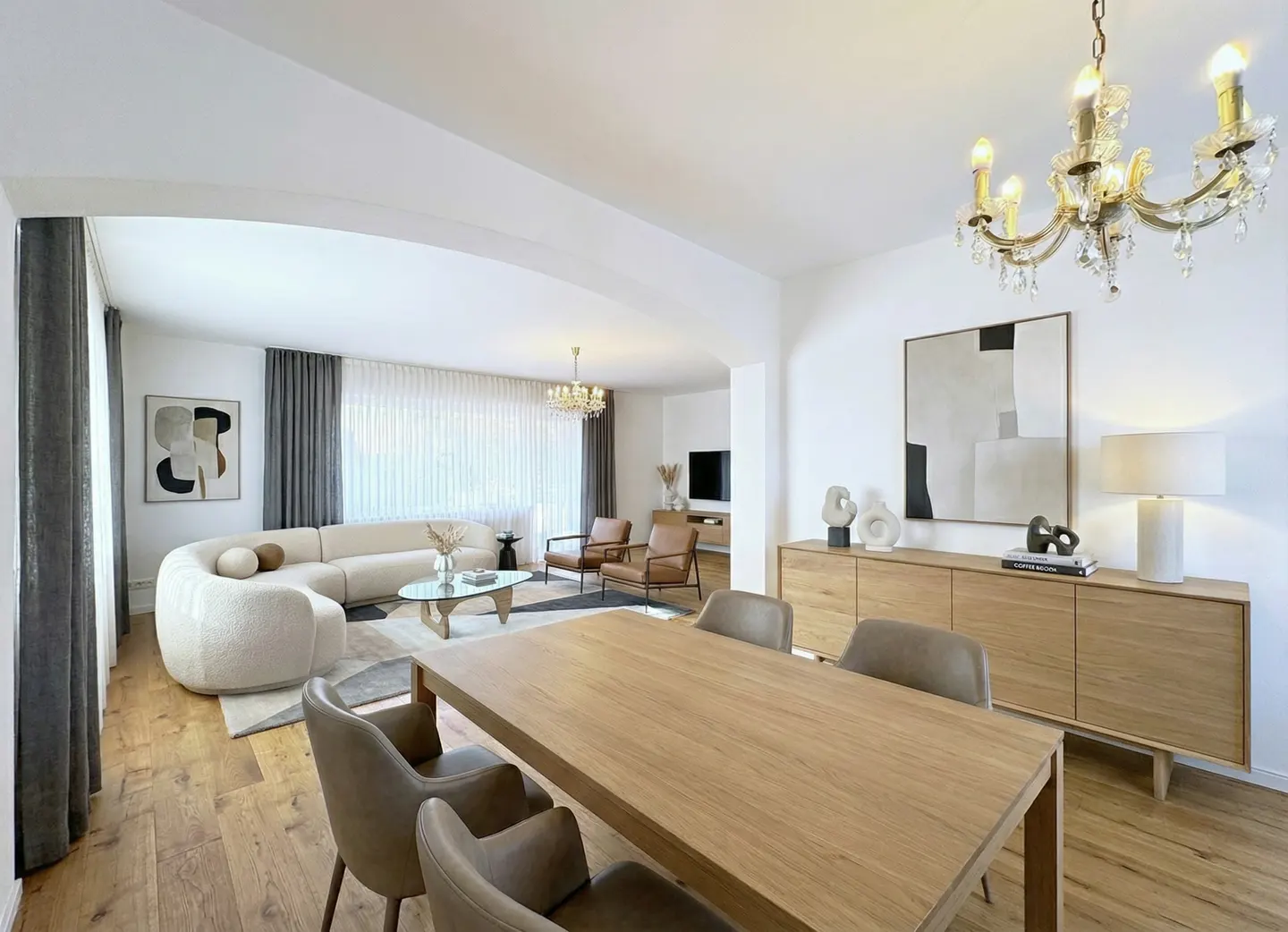 Bright, open-concept living and dining area with hardwood floors. A cream sofa, wood table, and chandelier create a modern, inviting space.
