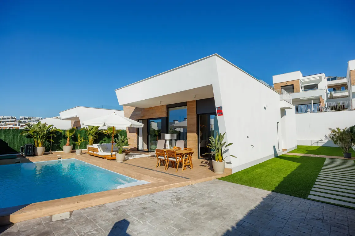 Modern white house with a pool, patio furniture, and green lawn under a clear blue sky.
