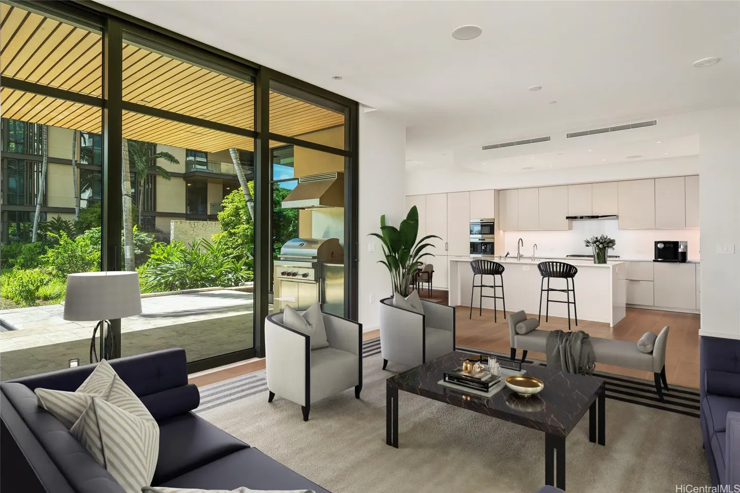 A modern living room with a blue sofa, gray chairs, and a marble coffee table. A kitchen is visible in the background. Large glass doors lead to a patio with a grill.